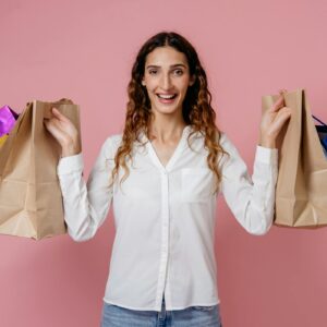 A joyful woman holding shopping bags against a pink studio background, expressing happiness and fashion.